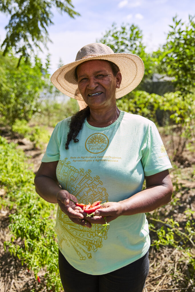 Agricultora de chapéu de palha sorrindo na roça com pimentas